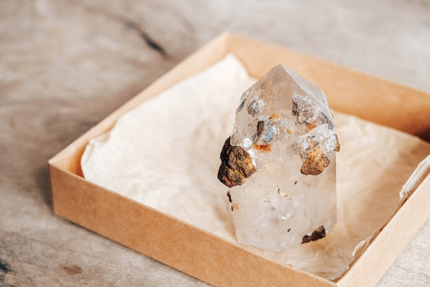 Quartz crystal in a kraft paper box on wooden background. Copy, empty space for text. - Photo, Image
