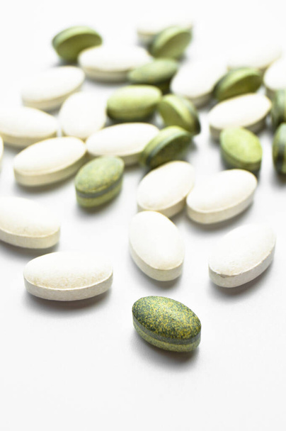 Bílé a zelené oválné tablety pilulky izolované na bílém pozadí, medicínské oválné tablety - Fotografie, Obrázek