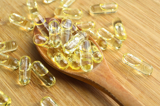 竹のまな板上の木製のスプーンで黄色の魚油楕円形の錠剤、医療楕円形の錠剤 - 写真・画像
