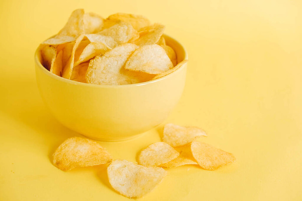 Картофельные чипсы в желтой миске на желтом фоне. Копирование, пустое место для текста. - Фото, изображение