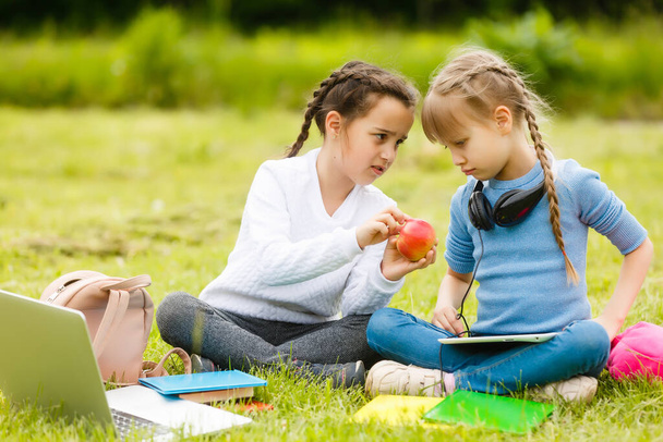 Uczniowie szkoły podstawowej z pudełkami na lunch w rękach. Dziewczyny z plecakami jedzą na trawniku. Zaczynamy lekcje. Pierwszy dzień jesieni. - Zdjęcie, obraz