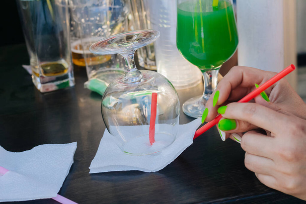 Бармен наливает зеленый абсент в красивые бокалы и поджигает их на уличной вечеринке. Стеклянные стаканы с алкоголем - Фото, изображение
