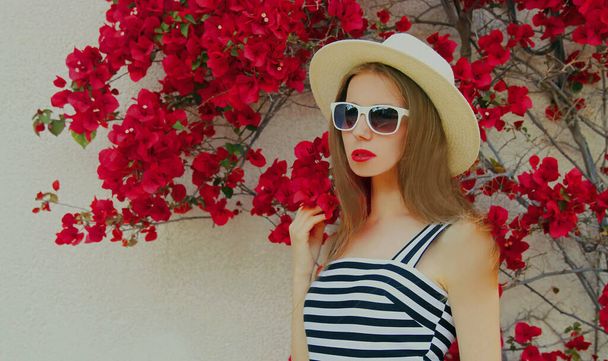 Portrait of beautiful woman wearing a summer straw hat on a red flowers background - Foto, Imagen