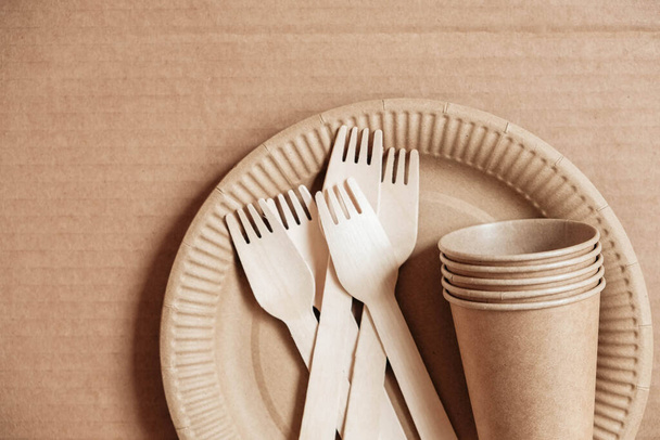 Wooden forks and paper cups with plates on kraft paper background. Eco friendly disposable tableware. Also used in fast food, restaurants, takeaways, picnics. Top view. Copy, empty space for text. - Foto, Imagen
