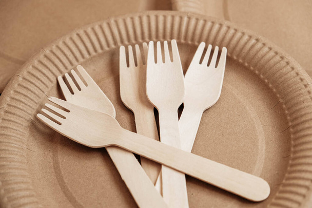 Wooden forks and plates on kraft paper background. Eco friendly disposable tableware. Also used in fast food, restaurants, takeaways, picnics. Top view. Copy, empty space for text. - Photo, Image