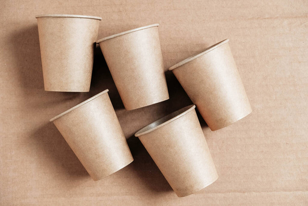 Disposable paper cups on kraft paper background. Eco friendly disposable tableware. Zero waste concept. Top view. Copy, empty space for text. - Photo, Image