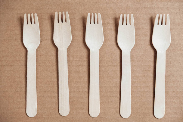 Wooden forks on a cardboard background. Eco friendly disposable tableware. Top view. Copy, empty space for text. - Fotó, kép