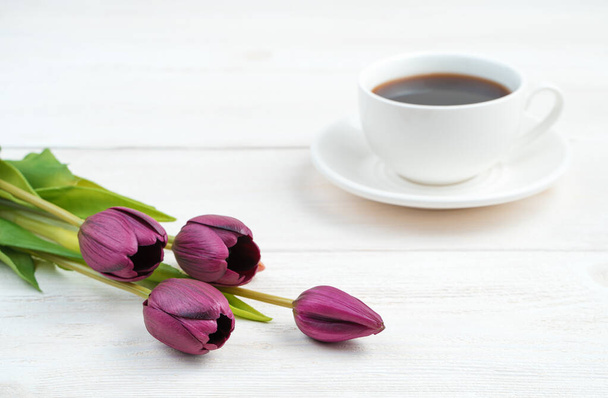 Fleurs violettes et une tasse de café blanc en arrière-plan sur un fond en bois clair. - Photo, image