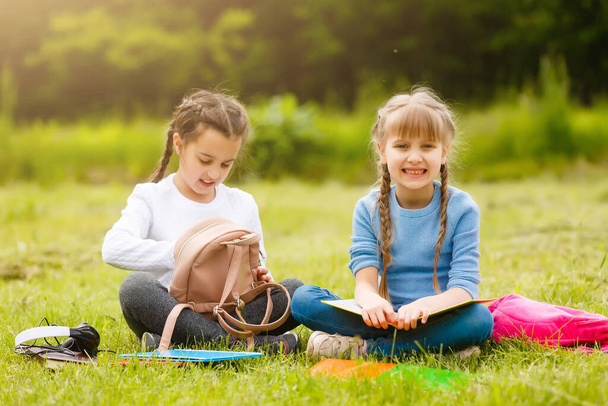 deux écolières multiculturelles mignonnes assis sur la pelouse sous l'arbre et le livre de lecture ensemble - Photo, image