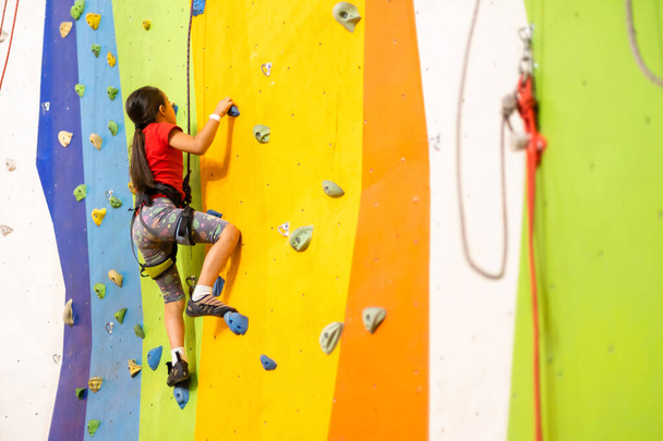 Sporty little girl climbing artificial boulder on practical wall in gym - Zdjęcie, obraz