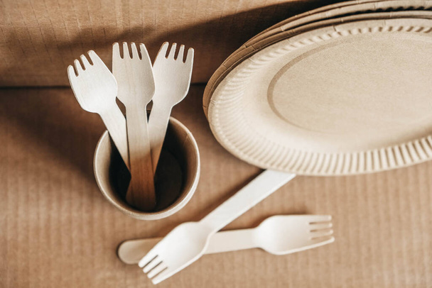 Wooden forks and paper cups with plates on kraft paper background. Eco friendly disposable tableware. Also used in fast food, restaurants, takeaways, picnics. Top view. Copy, empty space for text. - Photo, Image