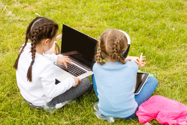 Dwie śmieszne uczennice siedzą na trawie i czytają książki. Dziewczyny, dziewczyny, siostry uczą się przyrody.. - Zdjęcie, obraz