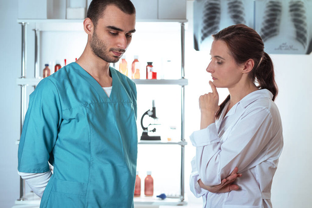 Zwei nachdenkliche müde Ärzte. Frau in weißem Laborkittel und Mann in medizinischer Kleidung. Lifestyle-Outdoor-Szene - Foto, Bild