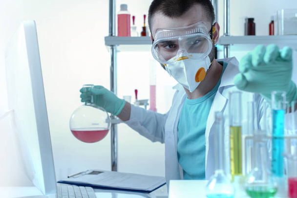 Un assistente chimico di laboratorio con occhiali protettivi e una maschera esamina le provette. - Foto, immagini