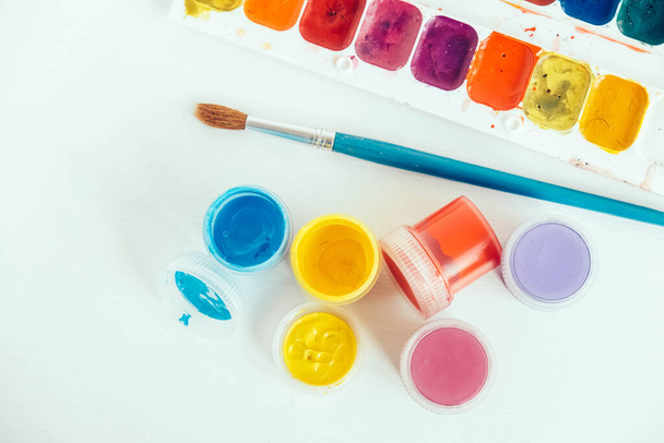 Πολύχρωμα χρώματα γκουάς και πινέλο για ζωγραφική σε λευκό ξύλινο τραπέζι. Στο πάνω μέρος. Αντιγραφή, κενό χώρο για κείμενο. - Φωτογραφία, εικόνα