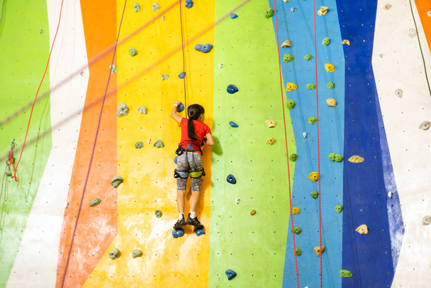 Pequeña niña escalada pared de roca pared práctica en el gimnasio - Foto, imagen