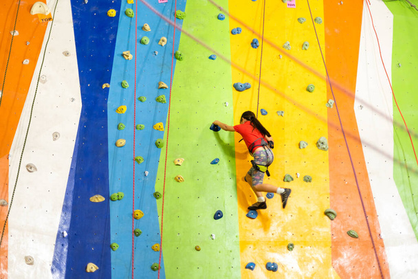 Sporty little girl climbing artificial boulder on practical wall in gym - Photo, Image