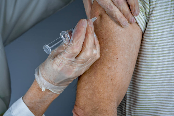 Доктор делает укол пожилому человеку в больнице. Медсестра держит шприц перед тем, как сделать Ковид-19 или коронавирусную вакцину. - Фото, изображение