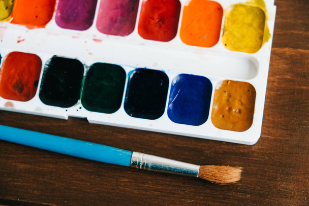 Set of watercolor paints with a brush for painting on a dark wooden background. Copy, empty space for text. - Foto, Imagen
