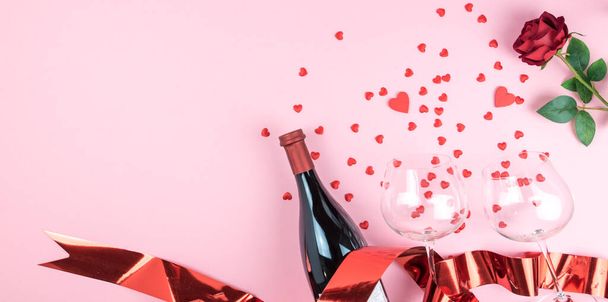 Valentinstag Grußkarte Vorlage. Rosa Hintergrund mit kleinen roten Herzen, Weinflasche mit Gläsern, rote Rose und rote Schleife. Kopierraum. Flache Lage, obere Lage - Foto, Bild