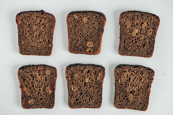 Slices of fresh brown bread with raisins on a white wooden background. Top view. Copy, empty space for text. - Фото, изображение