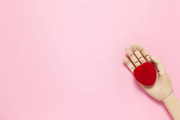 Wooden hand holds red small velvet heart shaped box for jewelry on pink background, copy space, flat lay. March 8, February 14, birthday, Valentine's, Mother's, Women's day celebration concept. - Fotografie, Obrázek