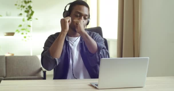 Afro american man student business person listening to music with headphones sitting at table in office or at home enjoying song singing dancing to melody sound enjoying rest break from work study - Footage, Video