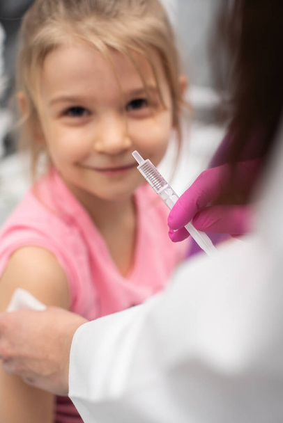 The girl is looking straight into the lens and the doctor is preparing a syringe for injection. Preventive vaccine for young children. - 写真・画像