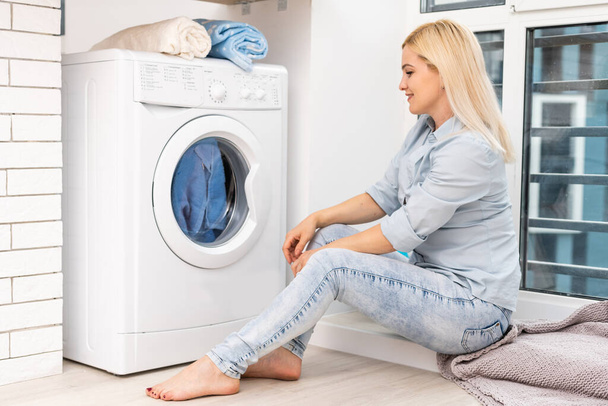 Çamaşır makinesi ve kıyafetleri olan genç bir ev hanımı. Yıkama Günü. - Fotoğraf, Görsel