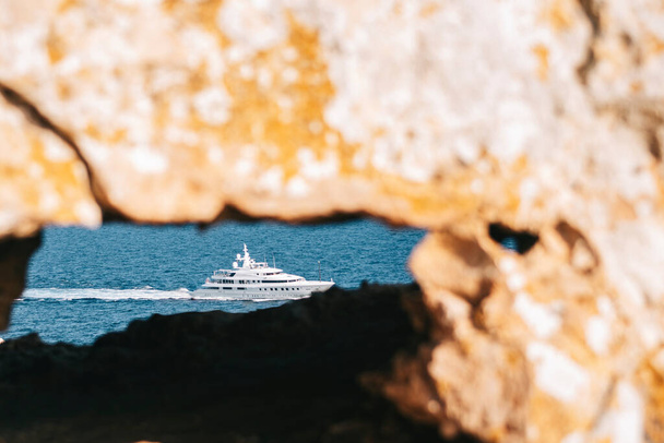Jacht, który przepływa morze i można zobaczyć przez dziurę w skale. - Zdjęcie, obraz