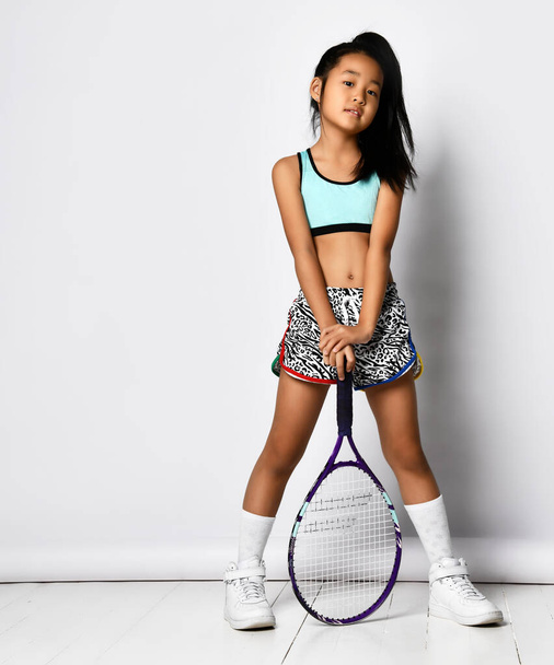 Badminton girl asian preteen model posing with racket full length portrait isolated on white. Young badminton or tennis player. Fashionable sportswear, sports and active childhood, healthy lifestyle - Фото, изображение