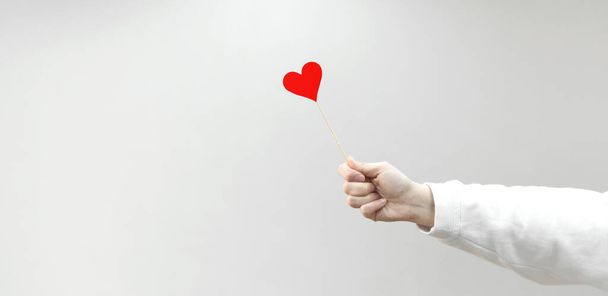 Símbolo de amor de memoria sobre un palo y mano femenina sobre fondo gris. banner con espacio de copia - Foto, imagen