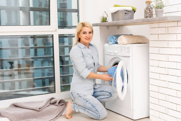 Uma jovem dona de casa com máquina de lavar roupa e roupas. Dia de lavagem. - Foto, Imagem