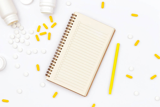 Open notepad and scattered pills on white table - Photo, Image
