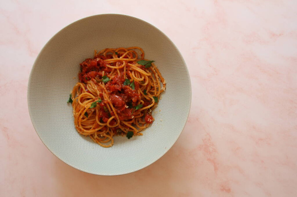 lautasellinen spagettia tomaattikastikkeessa, juustolla ja persiljalla siroteltuna, italialainen pasta-astia, yksinkertainen italialainen ruokalaji, hiilihydraatteja lautasella - Valokuva, kuva
