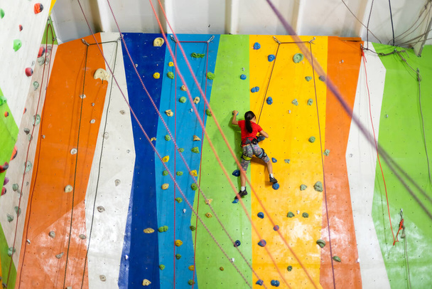 Sporty little girl climbing artificial boulder on practical wall in gym - Zdjęcie, obraz