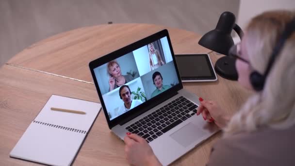 Женщина работает из дома, имея групповую видеоконференцию на ноутбуке - Кадры, видео