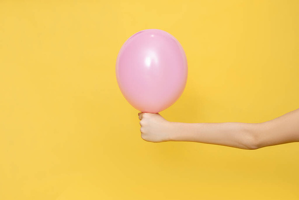 Lidská ruka drží jeden růžový balón na žlutém pozadí. Detailní studiová fotka. Oslavný koncept. Prázdné místo pro text. - Fotografie, Obrázek