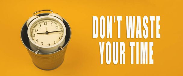 Don't waste your time concept with alarm clock and trash bin, banner on yellow background and inscription photo - Photo, Image