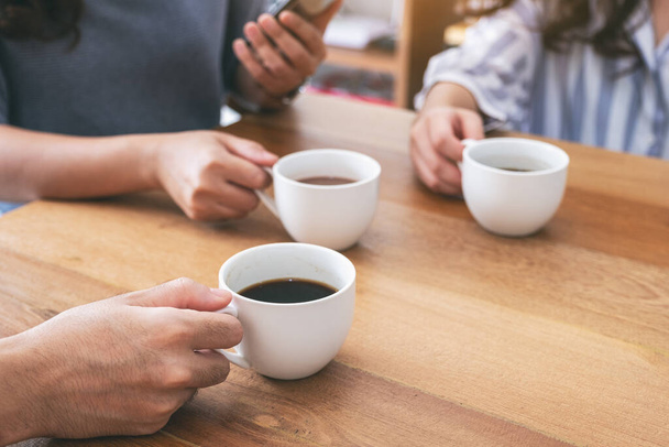 Closeup image of people using mobile phone and drinking coffee together - Photo, Image