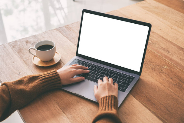 Immagine mockup di una donna che utilizza e digita sulla tastiera del computer portatile con schermo desktop bianco vuoto con tazza di caffè su tavolo di legno  - Foto, immagini