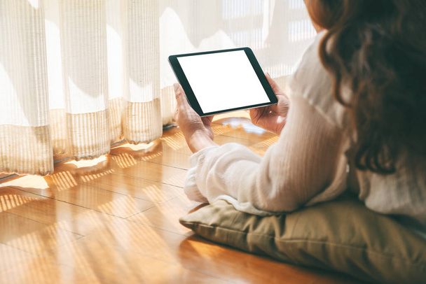 Mockup obrázek ženy držící černý tablet PC s prázdnou bílou desktopovou obrazovkou při ležení na podlaze s pocitem uvolněnosti - Fotografie, Obrázek