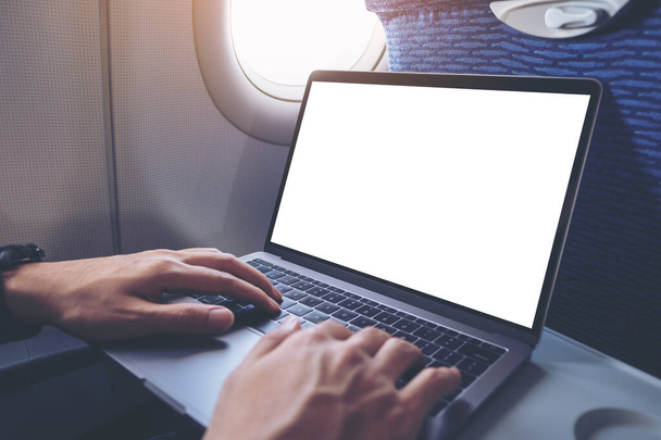 Immagine mockup di un uomo che usa e digita sul computer portatile con schermo bianco vuoto mentre è seduto in cabina - Foto, immagini
