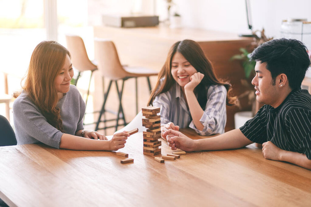 Три азиатских друзей сидя и играть Тамбл башня деревянный блок игры вместе с чувством счастья - Фото, изображение