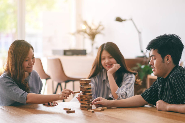 Three asian friends sitting and playing Tumble tower wooden block game together with feeling happy - 写真・画像