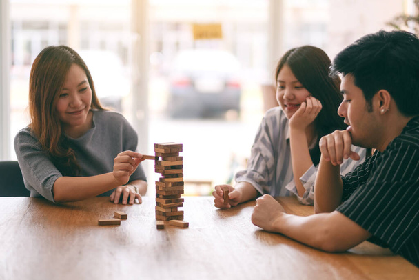 Three asian friends sitting and playing Tumble tower wooden block game together with feeling happy - Photo, image
