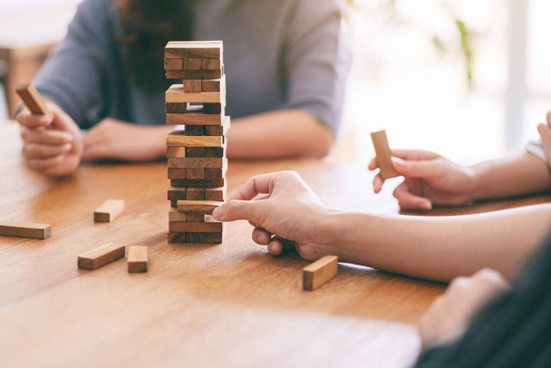 Closeup image of three friends sitting and playing Tumble tower wooden block game together - 写真・画像