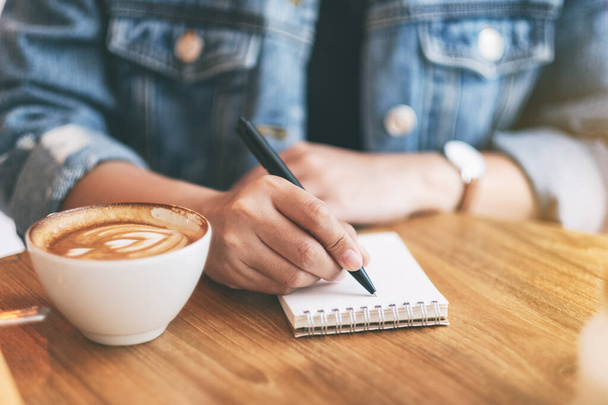 Крупный план женщины, пишущей на пустой блокнот с кофейной чашкой на деревянном столе - Фото, изображение