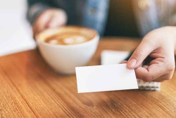 A woman holding and giving a blank empty business card to someone while drinking coffee - Фото, изображение