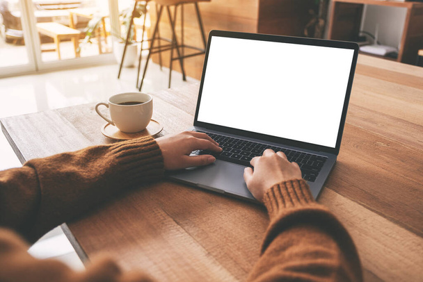Imagen burlona de la mano de una mujer usando y escribiendo en el portátil con pantalla de escritorio blanco en blanco con taza de café en la mesa de madera  - Foto, imagen